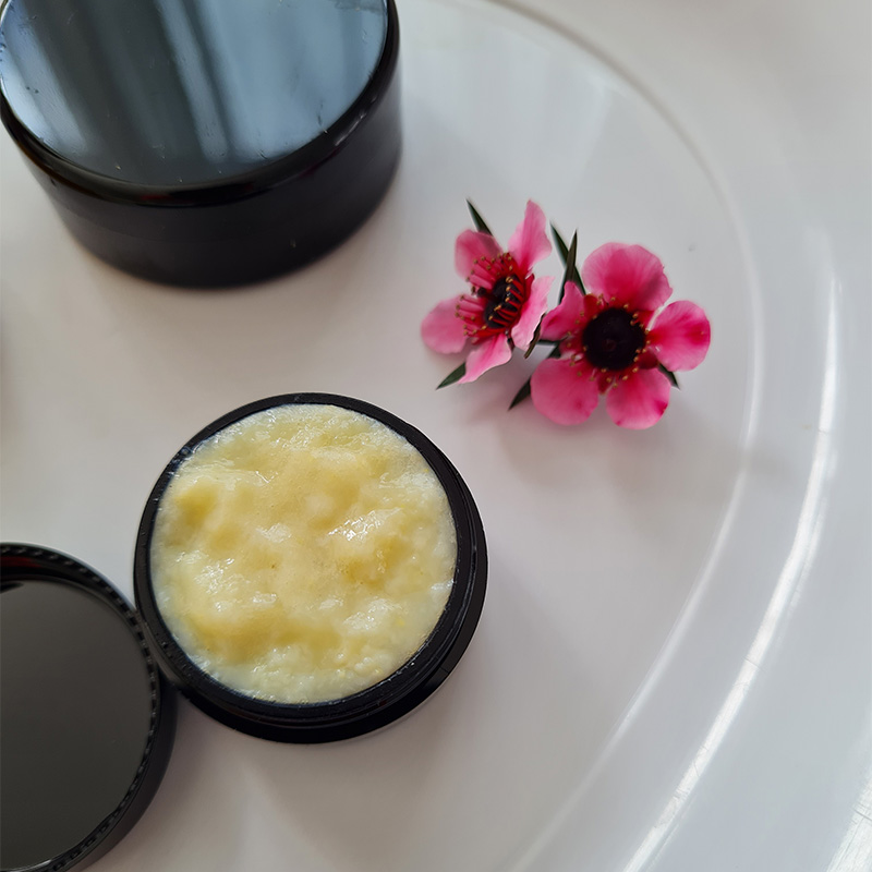 Open jar of creamy royal jelly next to pink flowers on a white plate